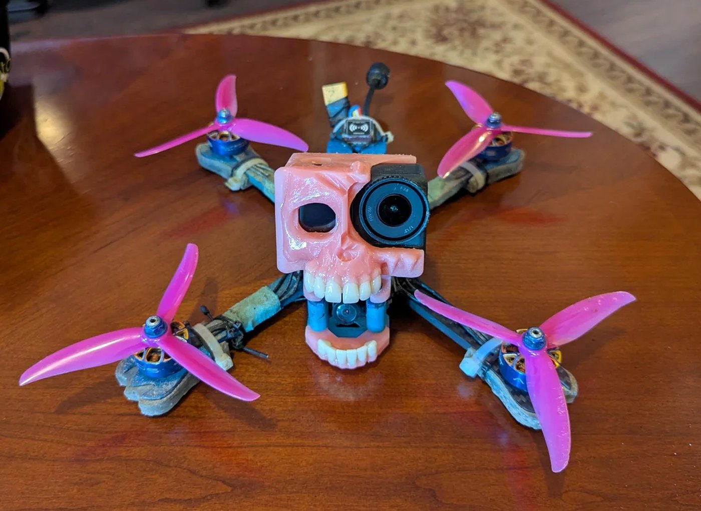 The FPV drone with Lucitone Digital Print denture canopy, pink tri-blade props, on a wooden table